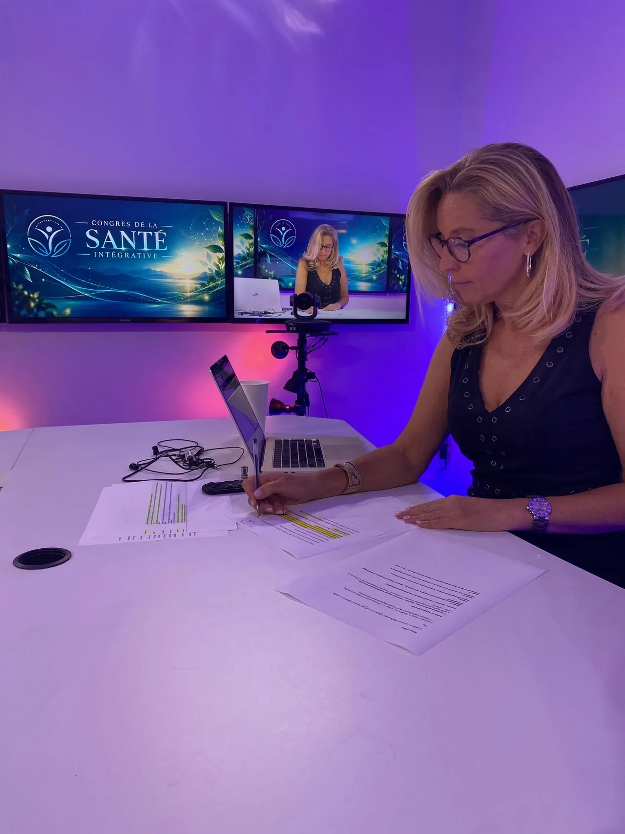 Une animatrice prépare son émission au desk, écrans habillés derrière elle