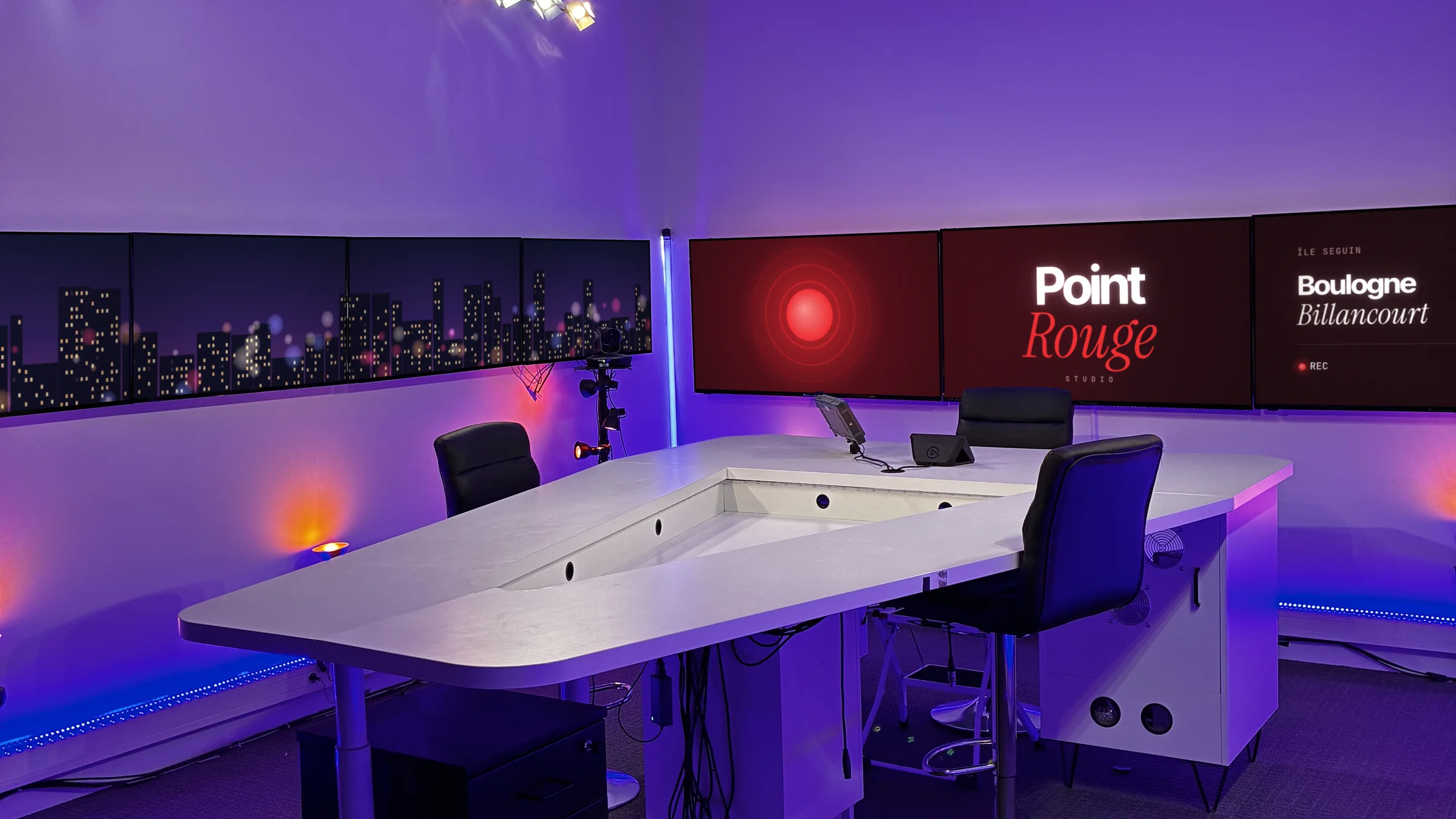 Le plateau Point Rouge Studio en lumière violette : desk blanc, mur d'écrans et régie